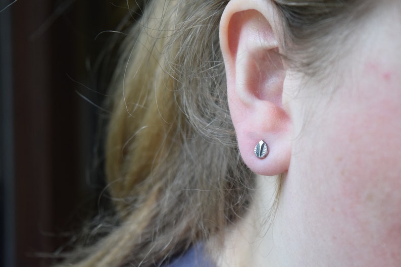 May include: A close-up of a person's ear with a small, silver stud earring. The earring has a textured, leaf-like design.