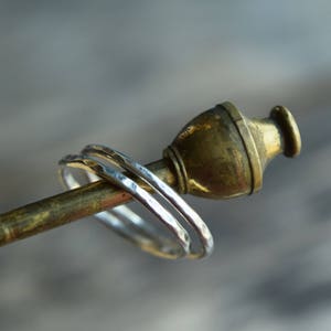 May include: Three silver hammered rings stacked on a brass display stand.