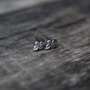 May include: A pair of silver flower stud earrings. The earrings are small and delicate, with a simple design.