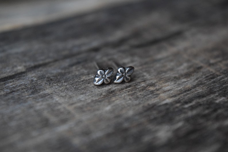 May include: A pair of silver flower stud earrings. The earrings are small and delicate, with a simple design.