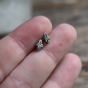 May include: A pair of silver flower stud earrings. The earrings are small and delicate, with a four-petal flower design.