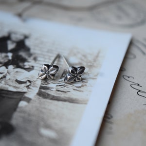 May include: A pair of silver flower stud earrings. The earrings are small and delicate, with a simple design.