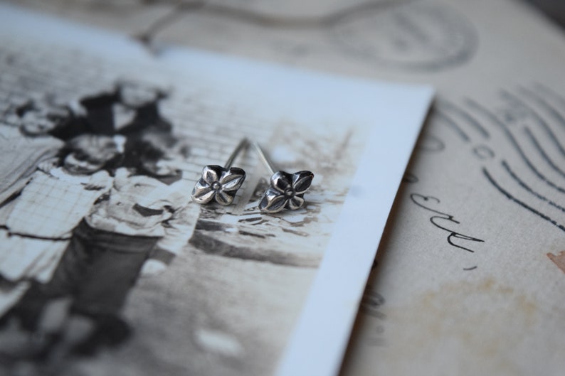 May include: A pair of silver flower stud earrings. The earrings are small and delicate, with a simple design.