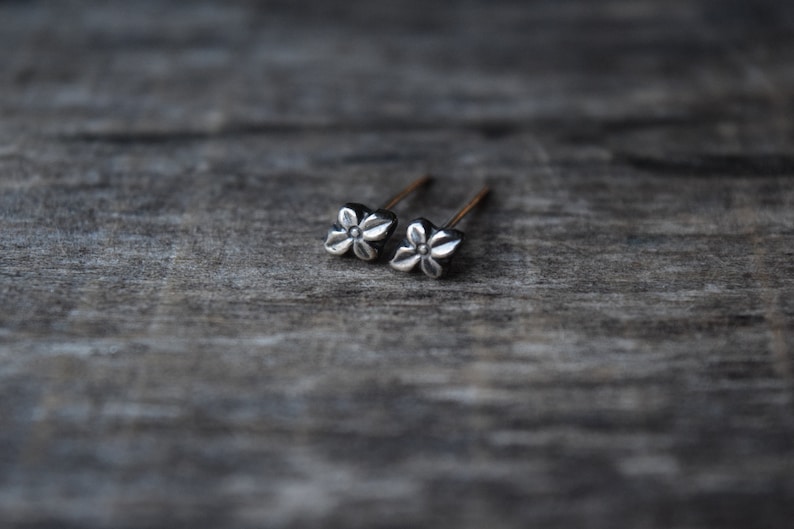 May include: A pair of silver flower stud earrings. The earrings are small and delicate, with a simple design.