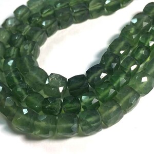 以下が含まれることがあります： ファセット加工された濃い緑色のビーズの連なり。各ビーズは、光を反射する複数のカット面を持つ立方体です。ビーズは一緒に紐でつながれており、ネックレスやブレスレットのコンポーネントを作成しています。ビーズのサイズは約1.3cmです。