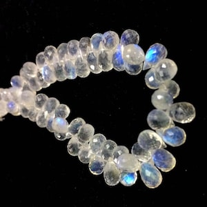 May include: A strand of white moonstone beads with iridescent blue flashes. The beads are teardrop shaped and strung on a clear thread.