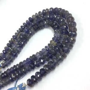 May include: A strand of dark blue faceted gemstone beads. The beads are oval shaped and have a slightly irregular shape. The beads are strung on a clear thread.