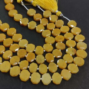 May include: A strand of yellow gemstone beads, each bead is faceted and has a hexagonal shape. The beads are strung on a white cord and have a yellow tassel.