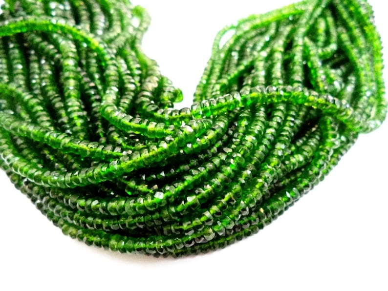 May include: Close-up of a collection of faceted, emerald green beads. The beads are strung together, creating a dense, textured appearance. The color is vibrant and the facets catch the light, giving them a sparkling effect.