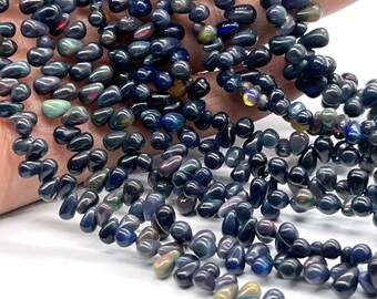 May include: A strand of dark blue teardrop-shaped opal beads. The beads have a iridescent sheen and are strung on a clear thread.