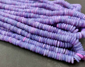 May include: A strand of purple and pink gemstone beads. The beads are small and round, and they are strung together on a clear thread. The beads are arranged in a pile, and they are all facing the same direction.