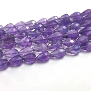 May include: A strand of purple amethyst gemstone beads in a faceted teardrop shape.