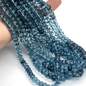 May include: Strands of small, round, translucent blue beads. The beads are strung together, creating a flowing, textured appearance. The beads are a deep, cool blue color, and the image is well-lit, highlighting the beads' subtle variations.