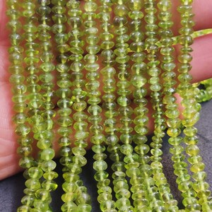 May include: A strand of green peridot beads, each bead is faceted and has a slightly rounded shape. The beads are strung on a clear thread and are approximately 4mm in diameter.