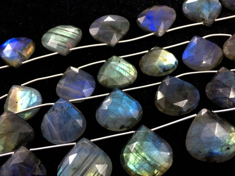 May include: A strand of iridescent labradorite gemstone beads in a teardrop shape. The beads are strung on silver wire and have a blue, green, and gold colour.