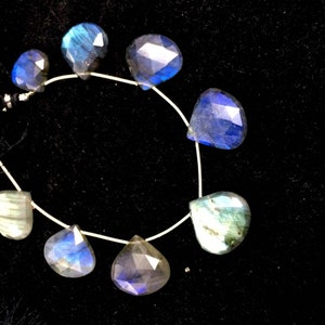 May include: A strand of faceted labradorite gemstone beads in shades of blue and green. The beads are teardrop shaped and strung on a silver wire.