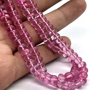 May include: A strand of pink tourmaline beads. The beads are round and have a smooth, polished finish. The beads are strung on a clear thread.
