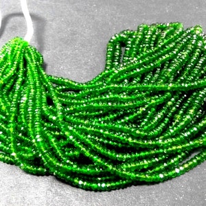 May include: A collection of bright green gemstone beads. The beads are small, faceted, and strung together, creating a flowing, textured appearance. The color is a vibrant, saturated green, with hints of lighter shades.