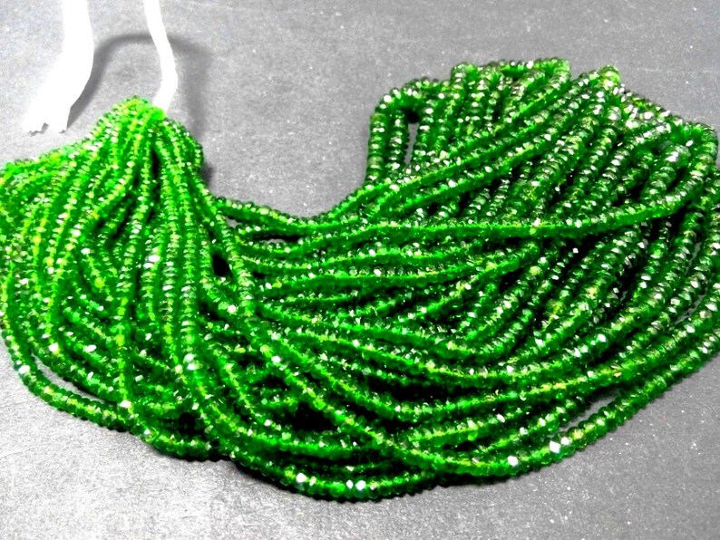 May include: A collection of bright green gemstone beads. The beads are small, faceted, and strung together, creating a flowing, textured appearance. The color is a vibrant, saturated green, with hints of lighter shades.
