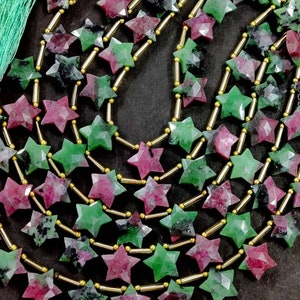 Könnte beinhalten: Eine Kette aus sternförmigen grünen und rosafarbenen Edelsteinperlen, die durch goldene Abstandshalter getrennt sind. Die Perlen sind facettiert und haben ein sternförmiges Muster.