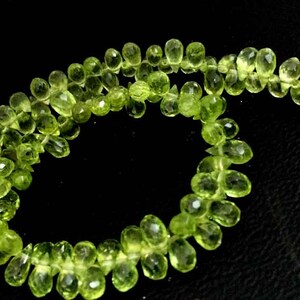May include: A strand of light green gemstone beads, likely peridot, strung together in a loose, flowing pattern. The beads are faceted and have a slightly irregular shape, giving the strand a natural, organic look.