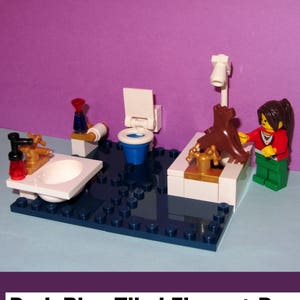 以下が含まれることがあります： レゴのバスルームのシーン。濃い青色のタイル張りの床、白い洗面台、トイレ、バスタブがあります。茶色の犬のフィギュアがバスタブの上にあります。画像には「Dark Blue Tiled Floors + Dog」と「No Minifigure Included」と書かれています。