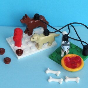 May include: A Lego playset featuring three toy dogs, a red fire hydrant, and a yellow bowl with red pieces. The dogs are brown, tan, and gray and white. Also included are white bone-shaped pieces.