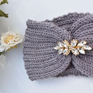 May include: Gray knitted headband with a gold and crystal embellishment. The headband is a simple, elegant design that can be worn with any outfit.