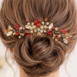 May include: A hair comb featuring a gold-toned wire frame adorned with faceted red and clear crystals. The design includes a central large red crystal surrounded by smaller clear and red stones arranged in a branch-like pattern across the comb.