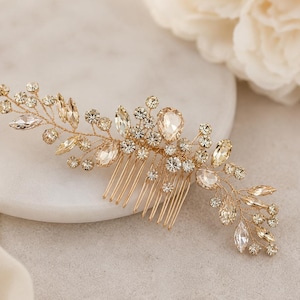 Könnte beinhalten: Ein goldfarbener Haarkamm mit einem filigranen, drahtgewickelten Design, verziert mit klaren und champagnerfarbenen Kristallen in verschiedenen Formen, darunter Marquise-, Rund- und Tropfenschliffe, angeordnet in einem floralen Muster.