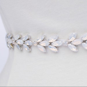 May include: A white bridal sash with a delicate design of silver leaves and clear iridescent crystals.