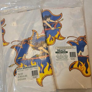 May include: Two plastic-backed table covers in clear packaging, each featuring a repeating graphic of Aladdin on a magic carpet against a blue and yellow flame design. The labels state the dimensions as 54 inches by 88 inches, or 3.3 square yards.