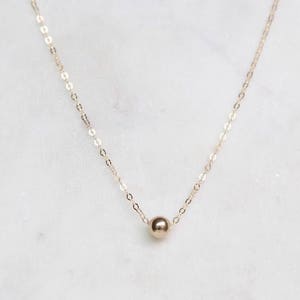 May include: A delicate gold chain necklace with a single, round gold bead pendant.