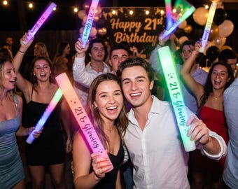 May include: A cylindrical LED foam glow stick featuring the text 21 & Glowing in black script with small star accents. The light-up party accessory emits a bright neon glow and is held upright by individuals at a nighttime celebration.