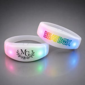May include: Two white translucent LED wristbands that emit a soft glow. One wristband features the text BEATBOX in a rainbow gradient font, while the other displays the letters MG surrounded by a black circular floral wreath design.
