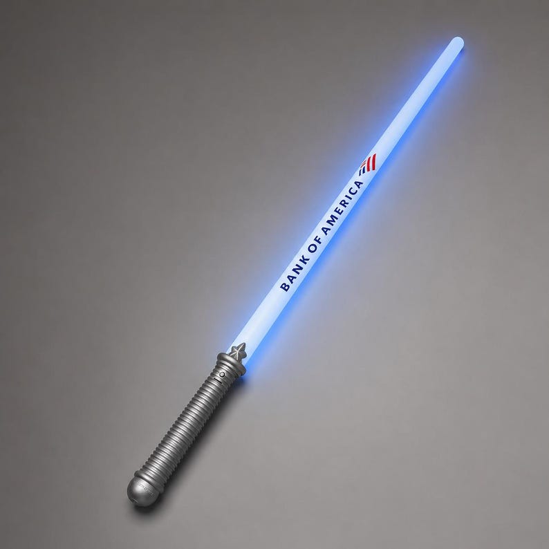 May include: A light-up toy sword with a silver-coloured ribbed handle and a glowing blue blade. The blade features the text BANK OF AMERICA printed in black along with the company's red, white, and blue flag logo near the top of the handle.
