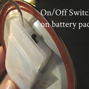 K&ouml;nnte beinhalten: Nahaufnahme eines wei&szlig;en Batteriefachs aus Kunststoff mit einem Ein-/Ausschalter. Der Schalter ist ein kleiner schwarzer Knopf.