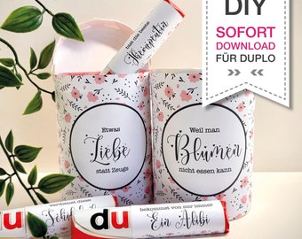May include: Two white cardboard tubes with pink floral patterns and text that reads "Etwas Liebe statt Zeugs" and "Weil man Blümen nicht essen kann".  A red and white candy bar with the text "du" and "Ein Alibi" is in the foreground.  The text "DIY SOFORT DOWNLOAD FÜR DUPLO » «" is in the background.
