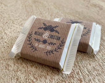 Pode incluir: Dois pequenos favores embrulhados em papel castanho com guarnição branca e uma faixa dourada. A frente do favor tem um desenho em preto e branco com o texto "Natalie & Christian" e "04 de agosto de 2020".