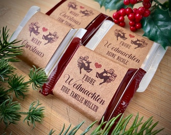 Pode incluir: Três barras de chocolate retangulares embrulhadas em folha de alumínio vermelho escuro com cintas de papel castanho personalizadas. Cada cinta apresenta um gráfico impresso de duas renas viradas para um coração vermelho e texto impresso.