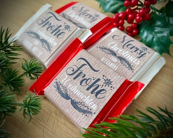 Pode incluir: Três barras de chocolate retangulares embrulhadas em folha de alumínio vermelha com etiquetas de papel personalizadas. As etiquetas de papel castanho texturado têm texto impresso a preto, incluindo Merry Christmas, Frohe Weihnachten e nomes.