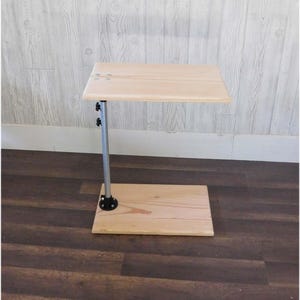 May include: A small wooden table with a metal stand. The table top is made of light wood and the stand is silver with black accents. The table is sitting on a wooden floor.