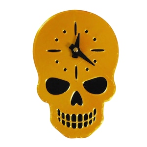 May include: A decorative wall clock in the shape of a skull. The clock is a vibrant gold color with black accents for the eyes and teeth. The clock hands are black. The clock measures approximately 7 inches in height and 5 inches in width.
