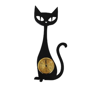 May include: A black cat-shaped wall clock with a gold-colored clock face. The clock has a minimalist design, with a long, slender body and a curved tail. The clock face displays the numbers 1 through 12.
