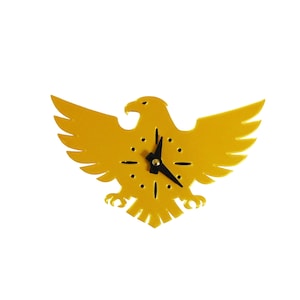 May include: A yellow eagle-shaped wall clock with black clock hands and hour markers. The clock has a gold finish and is designed in the shape of an eagle with outstretched wings. The clock's hands are black, and the hour markers are small black dots.