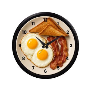 May include: A round wall clock with a black frame. The clock face features a breakfast plate with two fried eggs, bacon strips, and toast. The clock hands are black.