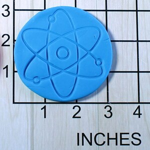 May include: A blue silicone mold shaped like an atom, measuring 2 inches in diameter. The mold is on a gridded surface with inch markings.