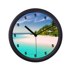 May include: A round black wall clock with a beach scene. The clock face features a turquoise ocean, white sand, and a blue sky with clouds. Black hands point to the time, and the numbers are marked with the number 5.