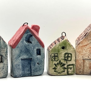 Pode incluir: Quatro pequenos ornamentos de cerâmica em forma de casa com argolas de metal para pendurar. As casas apresentam superfícies texturizadas em azul, verde e bege, com detalhes pintados à mão, incluindo janelas, portas, uma lua e motivos florais.