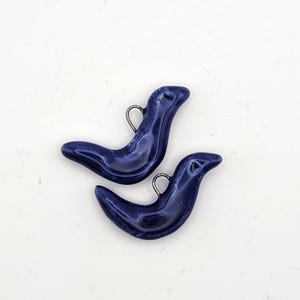 Puede incluir: Dos colgantes en forma de foca azul marino con acabado brillante y pequeños lazos metálicos para colgar. Los colgantes son lisos y tienen un diseño sencillo y elegante, ideal para joyería o proyectos de manualidades.